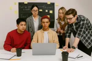 Group of young design professionals analyzing project plans on a laptop surrounded by notes and coffee