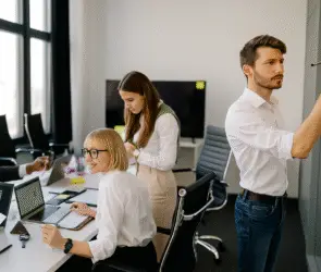 Design entrepreneur collaborating with team in growth mindset for the design business in a modern design studio office with laptops, documents, and sticky notes on a wall