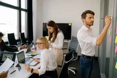 Design entrepreneur collaborating with team in growth mindset for the design business in a modern design studio office with laptops, documents, and sticky notes on a wall