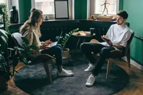 Two young design entrepreneurs discuss business ideas in a modern design studio with laptops and notepads.