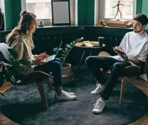 Two young design entrepreneurs discuss business ideas in a modern design studio with laptops and notepads.