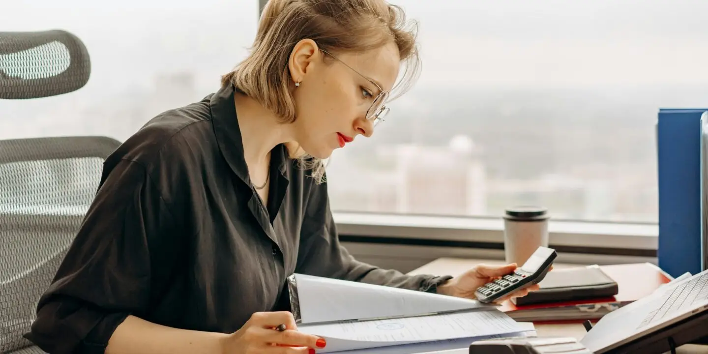 Focused design business woman calculating financial start-up cost at a desk with documents and office supplies