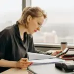 Focused design business woman calculating financial start-up cost at a desk with documents and office supplies