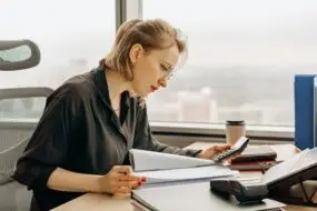 Focused design business woman calculating financial start-up cost at a desk with documents and office supplies