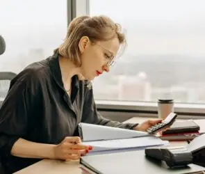 Focused design business woman calculating financial start-up cost at a desk with documents and office supplies