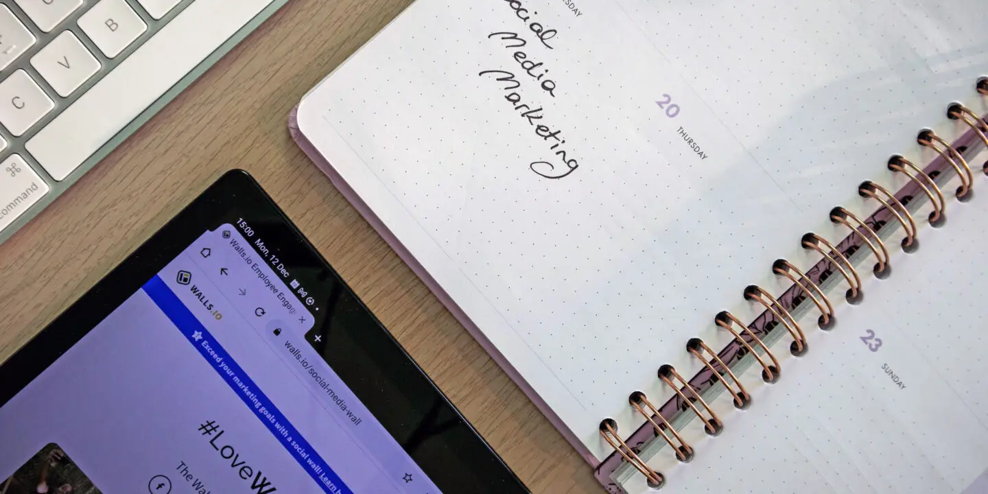 Social media content planner page beside keyboard and tablet displaying social wall