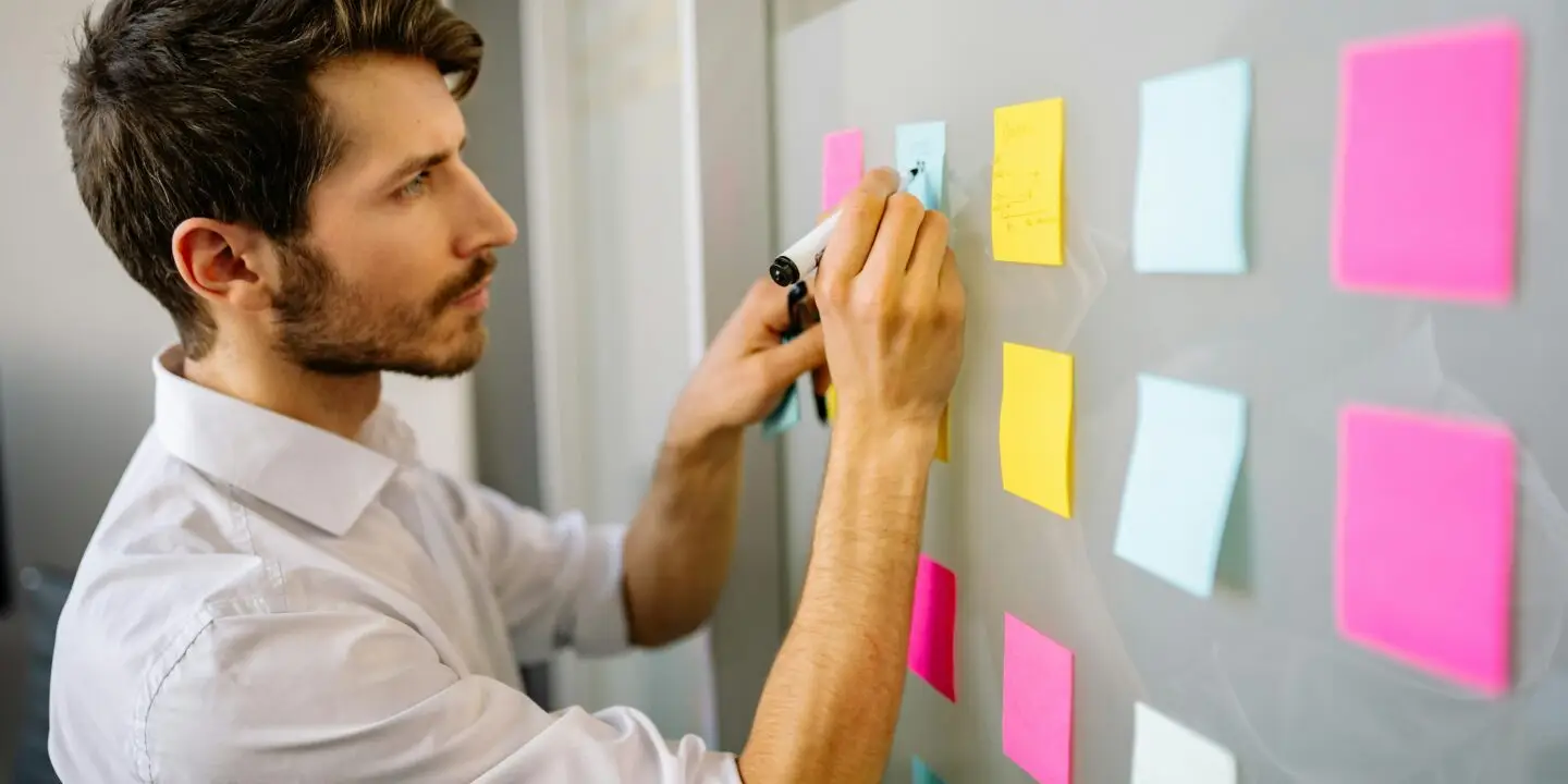 Focused design entrepreneur writing on colorful sticky notes during a business goal setting session.