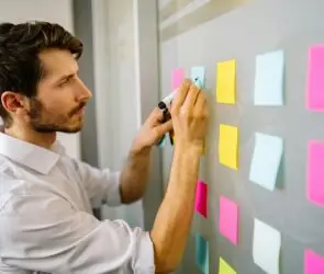 Focused design entrepreneur writing on colorful sticky notes during a business goal setting session.