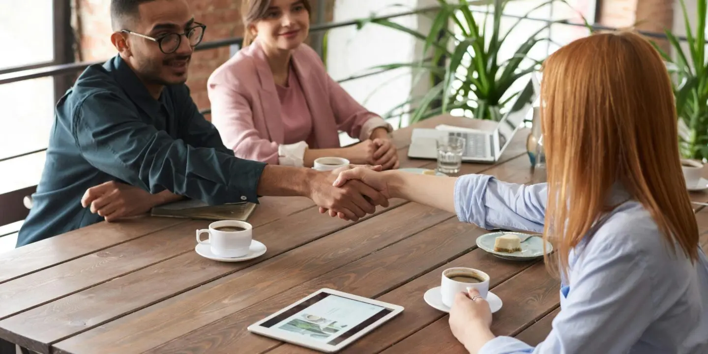 Design Entrepreneurs shaking hands during a related partnering business meeting in a relaxed, coffee shop workspace.