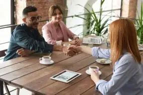 Design Entrepreneurs shaking hands during a related partnering business meeting in a relaxed, coffee shop workspace.