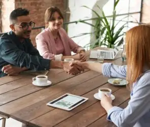 Design Entrepreneurs shaking hands during a related partnering business meeting in a relaxed, coffee shop workspace.
