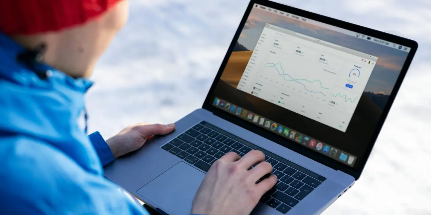 Design entrepreneur person in a red beanie using a laptop outdoors to track business social media analytics on a dashboard.