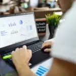 Design Entrepreneur working on a laptop with colorful financial goals strategy data charts and graphs displayed on screen.