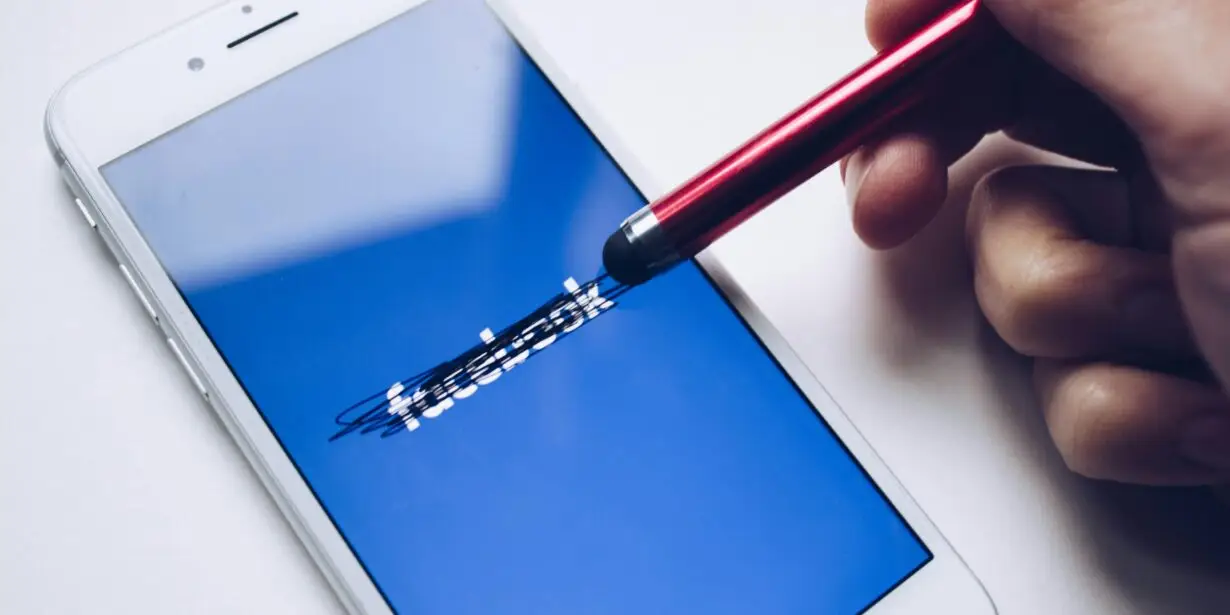 Stylus scratching out Facebook logo on smartphone screen, suggesting rethinking social media strategy for a design business.