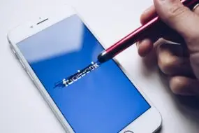 Stylus scratching out Facebook logo on smartphone screen, suggesting rethinking social media strategy for a design business.