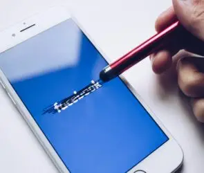Stylus scratching out Facebook logo on smartphone screen, suggesting rethinking social media strategy for a design business.