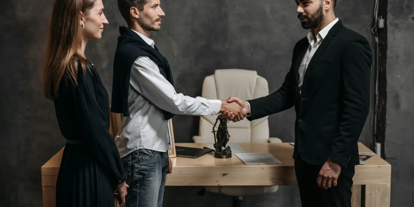 Two design business entrepreneurs finalize a referred deal with a handshake in a modern design studio office.
