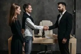 Two design business entrepreneurs finalize a referred deal with a handshake in a modern design studio office.
