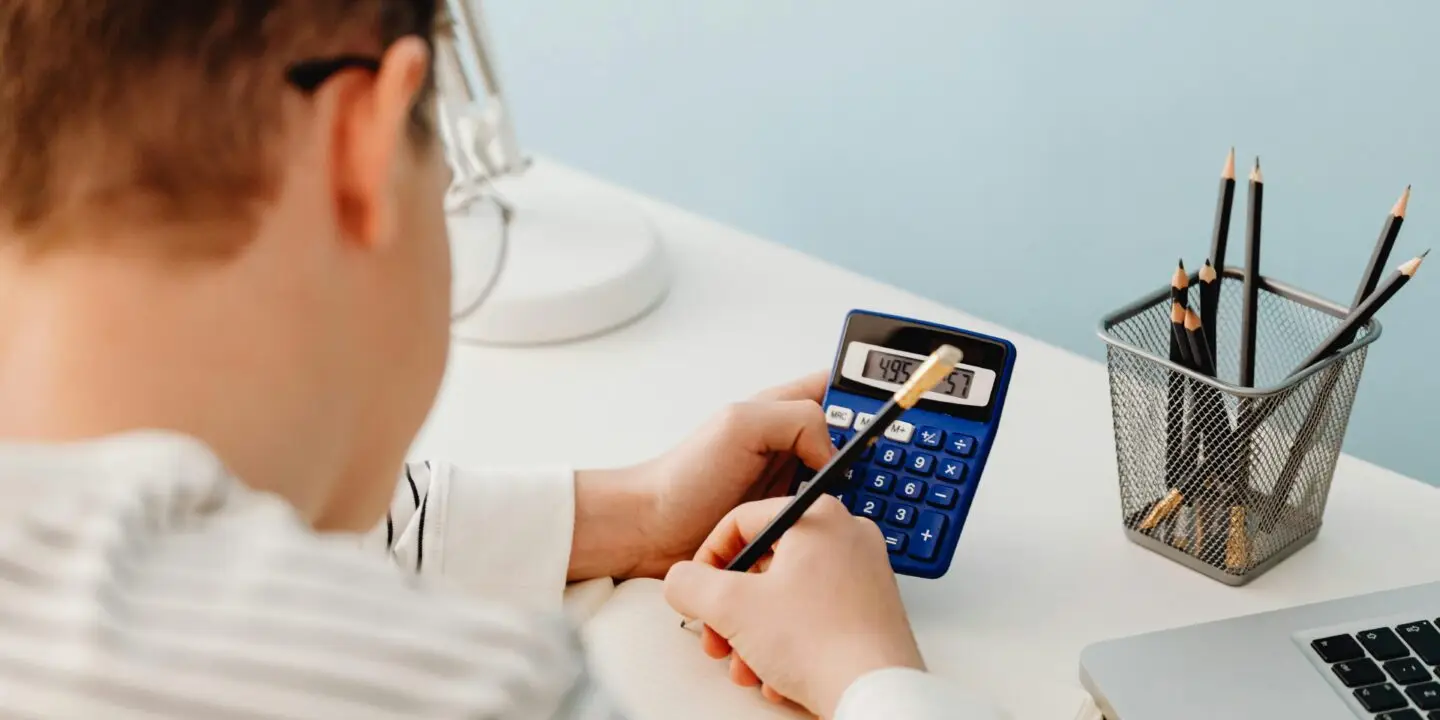 Design entrepreneur calculating financial numbers with a blue calculator and pencil at a modern white desk.