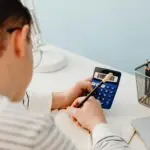 Design entrepreneur calculating financial numbers with a blue calculator and pencil at a modern white desk.