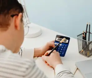 Design entrepreneur calculating financial numbers with a blue calculator and pencil at a modern white desk.