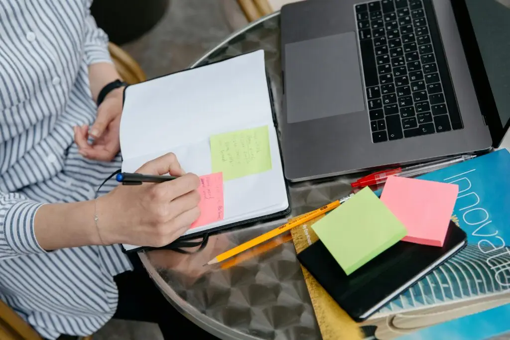 Design entrepreneur writing notes on colorful sticky pads with a laptop and business books on a glass desk
