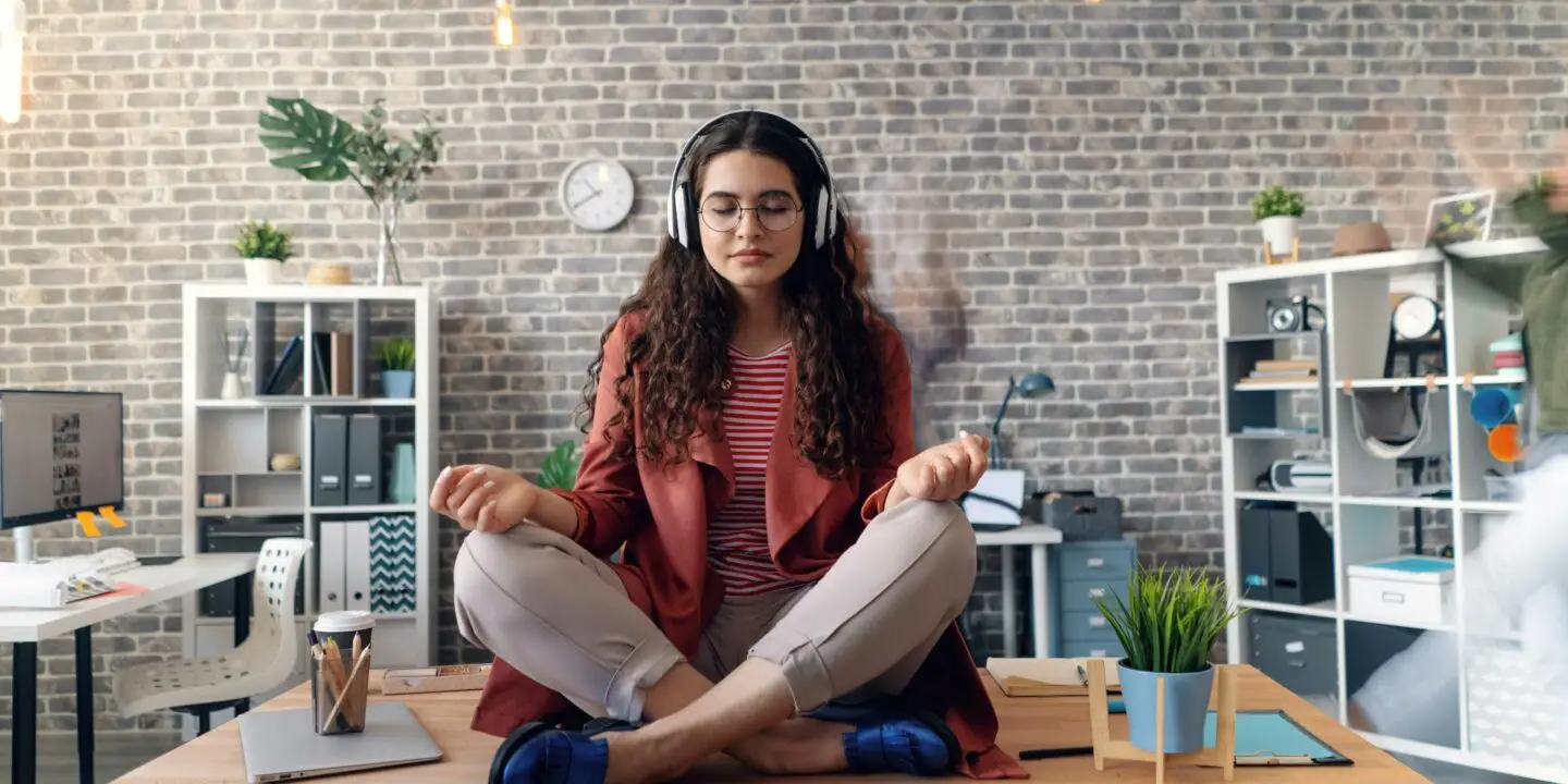Female creative design entrepreneur practicing mindfulness at work with headphones and meditation