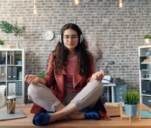 Female creative design entrepreneur practicing mindfulness at work with headphones and meditation