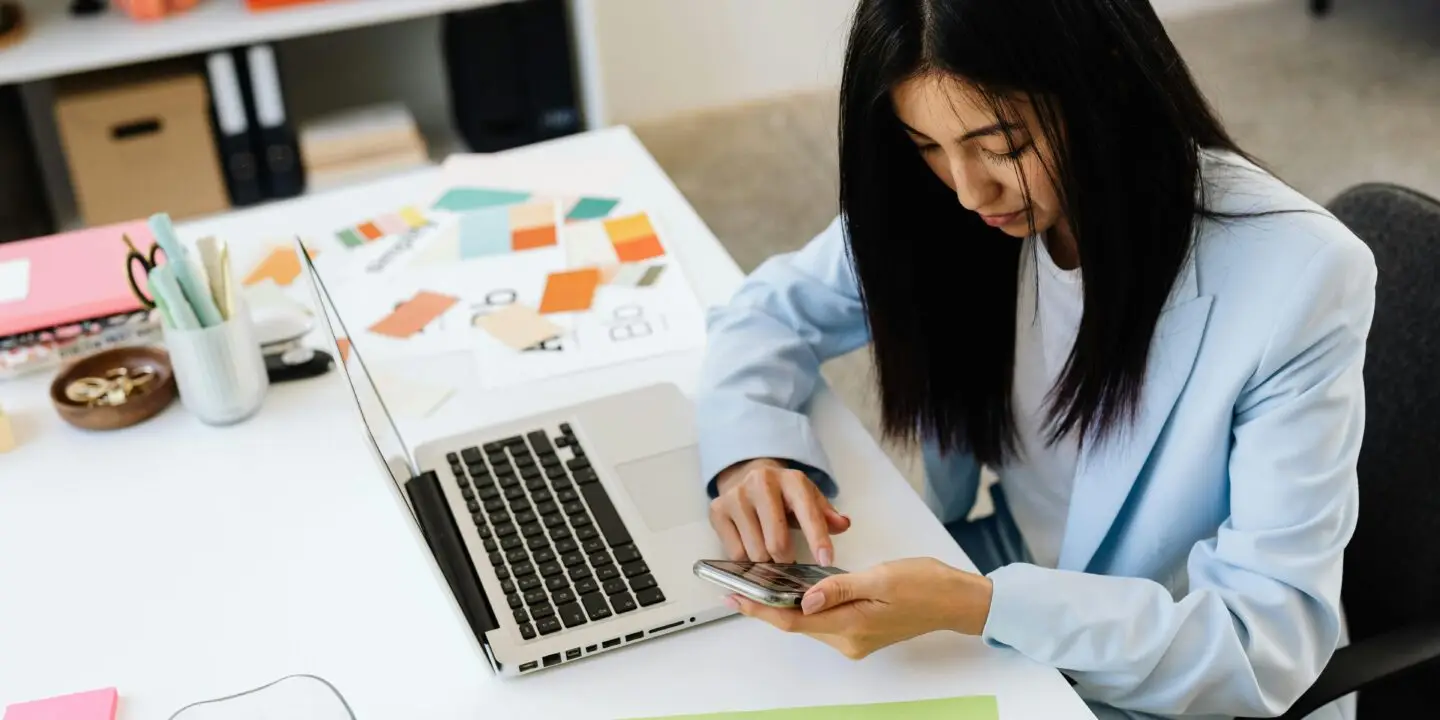 Female design entrepreneur checking mobile branding at a desk with brand design layouts and color palettes
