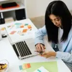 Female design entrepreneur checking mobile branding at a desk with brand design layouts and color palettes