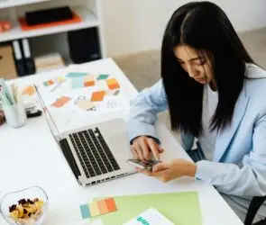 Female design entrepreneur checking mobile branding at a desk with brand design layouts and color palettes