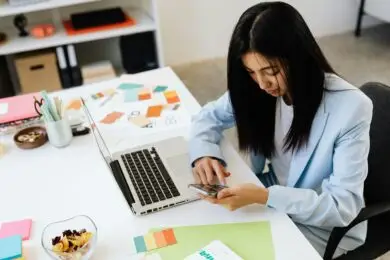 Female design entrepreneur checking mobile branding at a desk with brand design layouts and color palettes