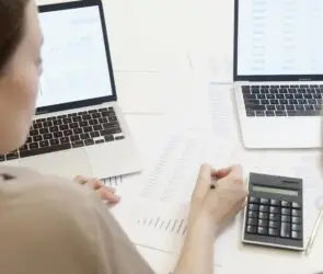 Two design entrepreneurs reviewing financial reports with laptops and calculator to manage design business budgets.