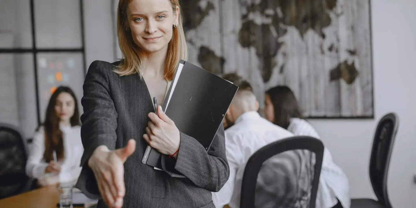 Confident businesswoman smiling and extending her hand for a handshake during a design client meeting.