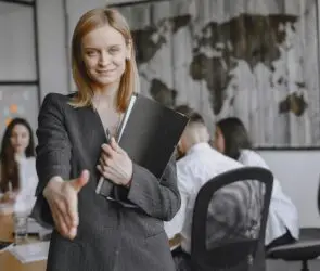 Confident businesswoman smiling and extending her hand for a handshake during a design client meeting.