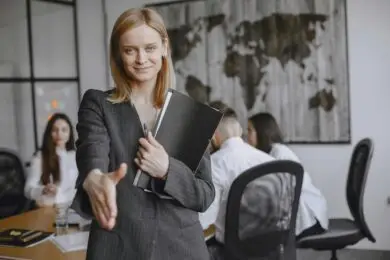 Confident businesswoman smiling and extending her hand for a handshake during a design client meeting.