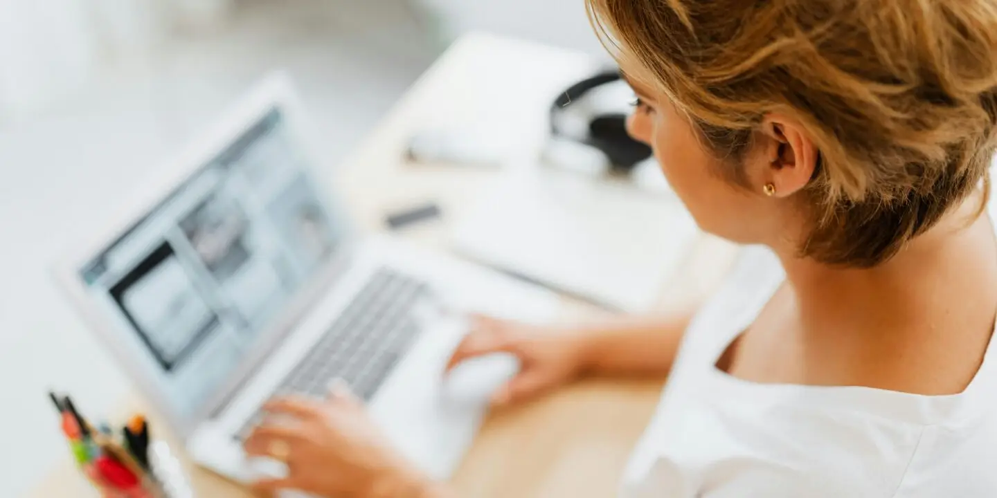 Woman design entrepreneur working on a laptop creating design packages for clients in a bright home office.