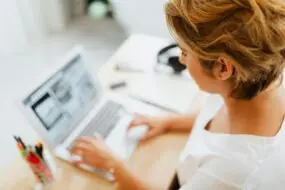 Woman design entrepreneur working on a laptop creating design packages for clients in a bright home office.