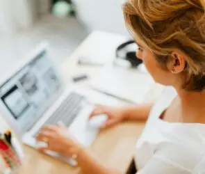Woman design entrepreneur working on a laptop creating design packages for clients in a bright home office.