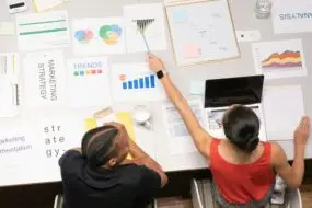 Two design entrepreneurs reviewing charts, graphs, and trend reports for a social media strategy meeting.