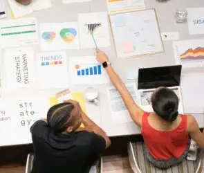 Two design entrepreneurs reviewing charts, graphs, and trend reports for a social media strategy meeting.