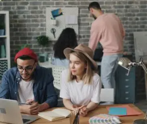 Designers collaborating in a creative design studio while reviewing marketing visuals and brand materials with AI on a laptop.