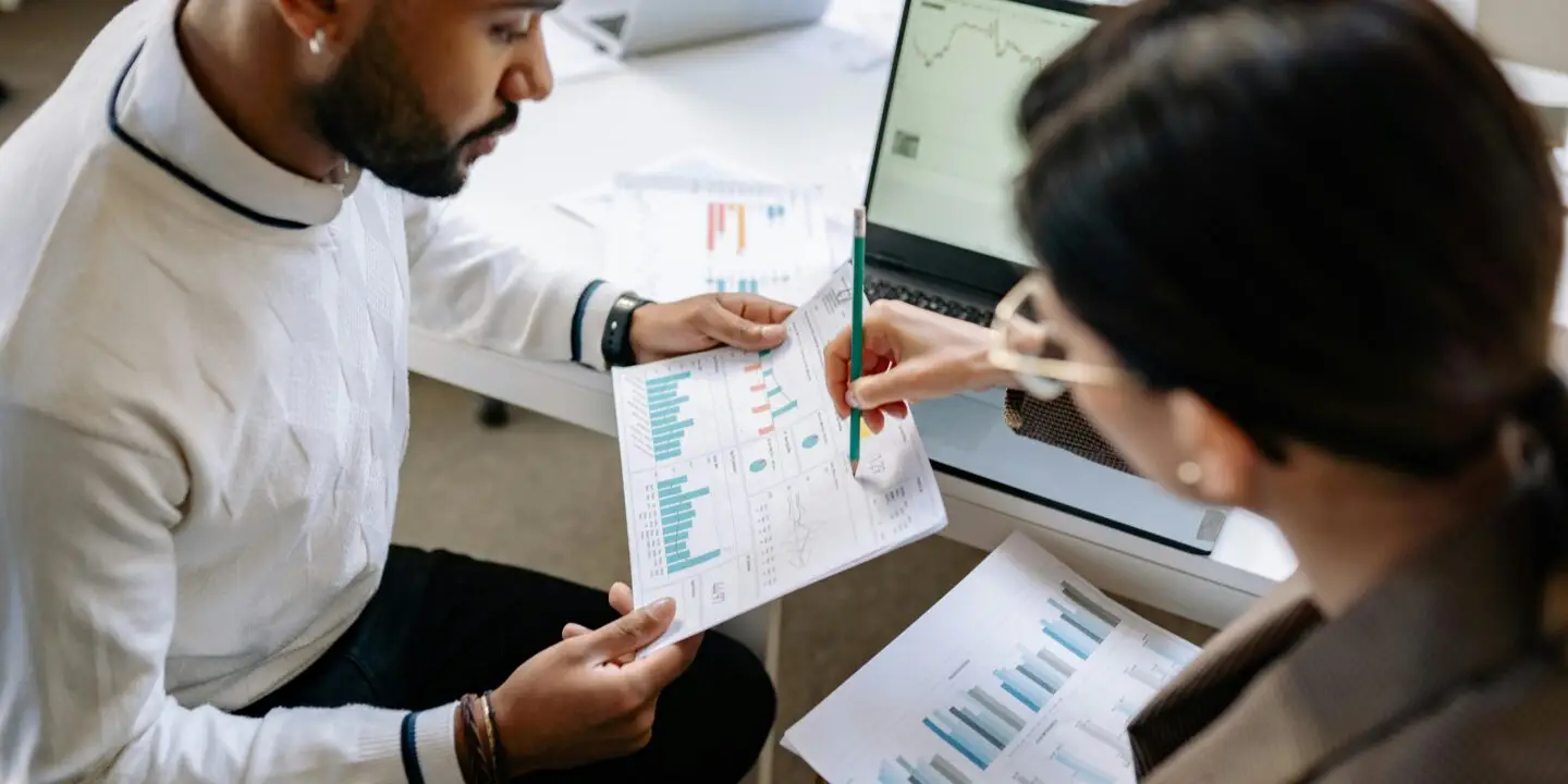 Design entrepreneur analyzing printed charts and graphs with a laptop to assess financial growth and business performance.