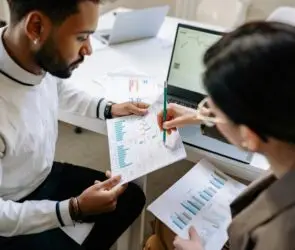 Design entrepreneur analyzing printed charts and graphs with a laptop to assess financial growth and business performance.