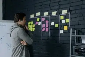 Freelancer planning workflow on a wall covered with sticky notes, organizing project stages for productivity and progress tracking.