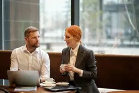 Designer and client working on project planning and cost estimation at a laptop in a home workspace.