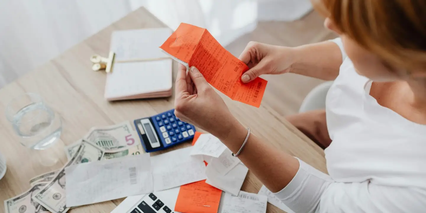 Designer reviewing receipts, cash, and calculator at desk.