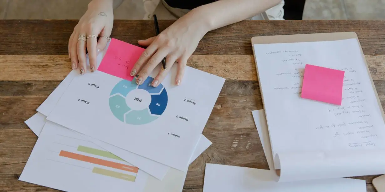 Designer reviewing strategy charts and notes on a wooden desk, analyzing workflow stages and project timelines for creative business planning.