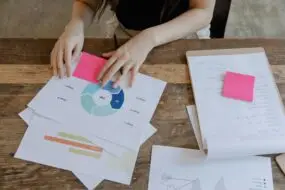 Designer reviewing strategy charts and notes on a wooden desk, analyzing workflow stages and project timelines for creative business planning.