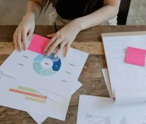 Designer reviewing strategy charts and notes on a wooden desk, analyzing workflow stages and project timelines for creative business planning.
